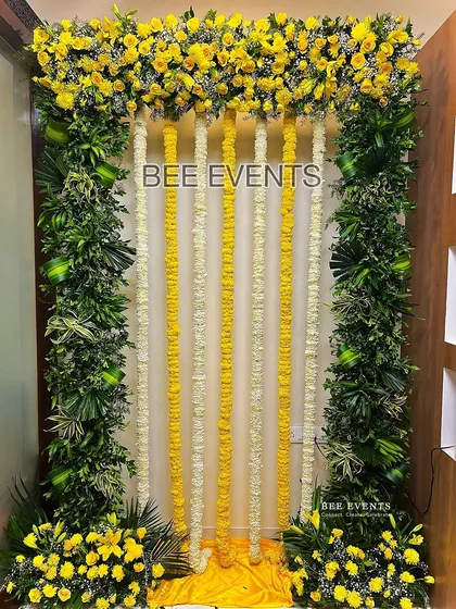 A simple and elegant Haldi backdrop perfect for an indoor celebration. The design features a frame of lush greenery and yellow flowers, with hanging garlands of tuberose and marigold.