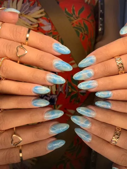 A full view of the serene blue marble nail art, styled with gold rings.