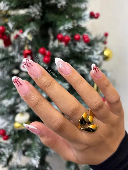 A delicate and festive take on the French manicure, with hand-painted red bows and a snowflake on a classic white tip.