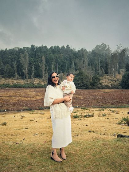 A joyful, candid shot of me holding Gauri in a beautiful open field in Ooty. This image radiates happiness and the simple joys of being a mom, making it perfect for campaigns focused on authentic family moments.