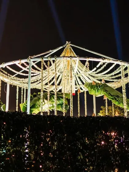 The view of the minimal floral mandap at night, illuminated to create a dramatic and romantic effect. The structure stands out beautifully against the dark sky.