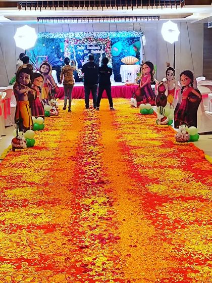 A long flower petal carpet creating a vibrant walkway for a Krishna-themed naming ceremony, lined with character cutouts to delight guests as they arrive.
