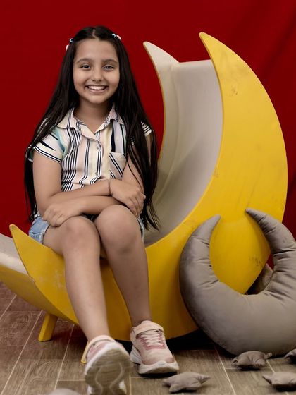 A dreamy "Love you to the moon and back" theme. This older girl is sitting on a large crescent moon prop against a bold red background, creating a striking and whimsical portrait.