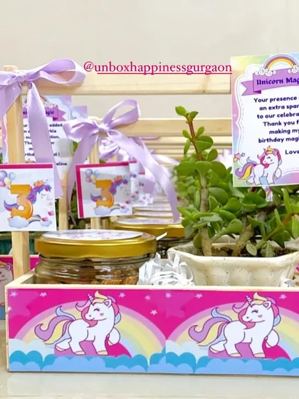 A close-up of a unicorn-themed return gift for a third birthday, featuring a jade plant, a jar of treats, and a personalized thank you card.