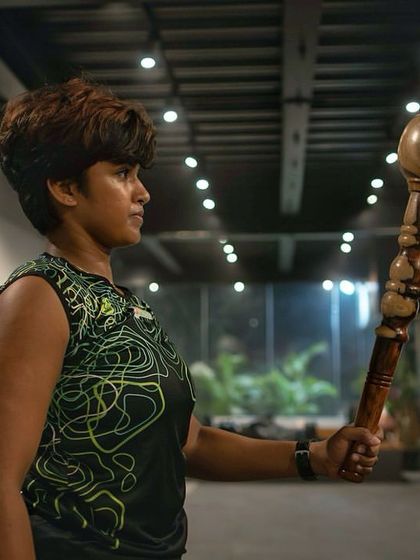 A female member holds a Gada with a look of intense focus. This image tells a story of dedication and the journey towards achieving personal fitness goals with us.