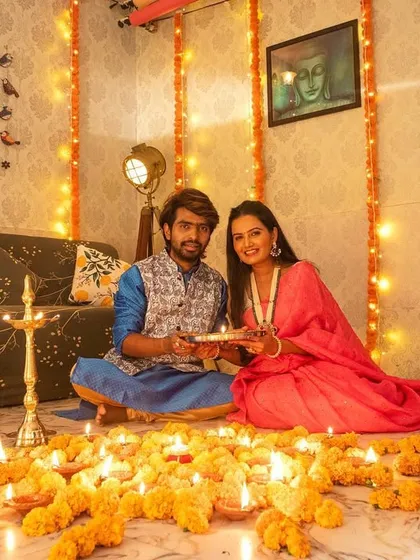 A classic couple portrait from a Diwali shoot, both looking at the camera while holding a thali, surrounded by the warm light of diyas.
