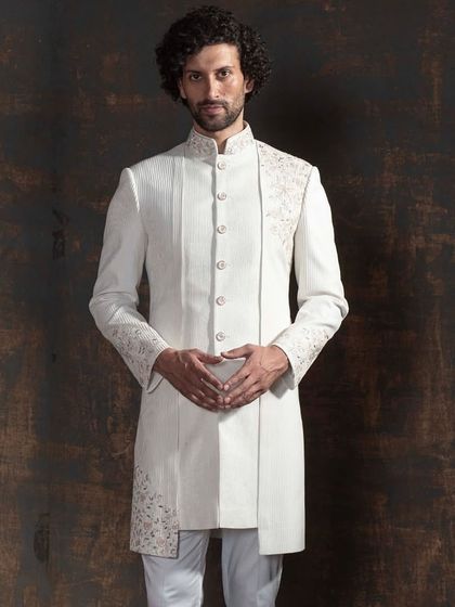This ivory sherwani is a statement in modern minimalism. The design features an asymmetrical cut with selective, delicate embroidery on the shoulder, cuff, and hem. It is for the groom who appreciates clean lines and a sharp, contemporary silhouette.