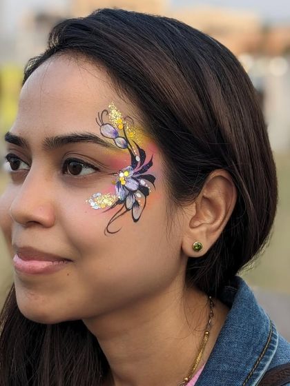 An intricate floral design with a rainbow background and gold glitter, a truly stunning piece of face art.