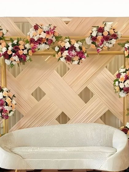 A minimalist yet elegant stage with a woven, textured backdrop. The design is accented with carefully placed bouquets of peach and burgundy flowers for a touch of color.