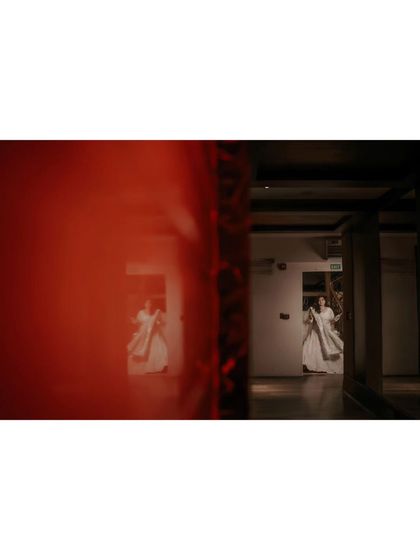 An artistic, wide-angle shot of the bride in a hallway. The use of a red foreground element to frame her adds a creative and cinematic touch.
