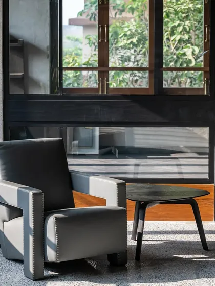 A quiet corner in the '9PM' residence. The simple, strong lines of the armchair and side table create a moment of pause, with natural light from the window highlighting the textures of the terrazzo floor and the wall.