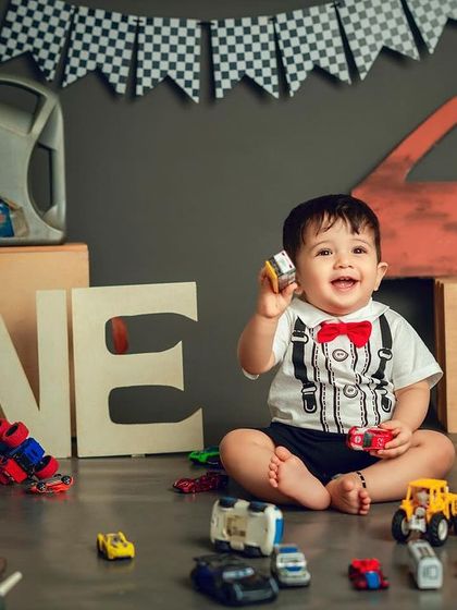 A big smile for his first birthday. The 'ONE' sign and toy cars complete this adorable and personalized mechanic-themed setup.