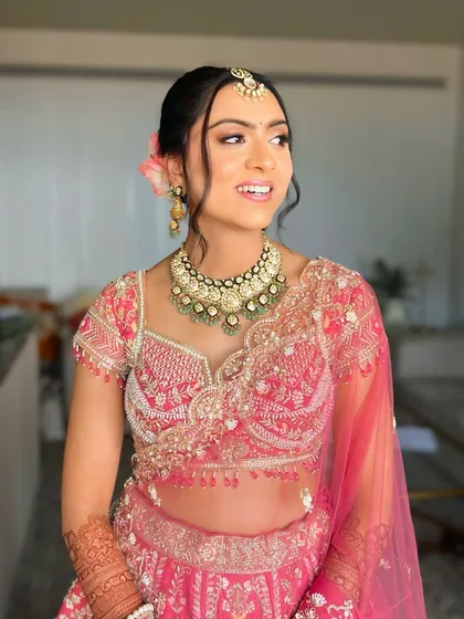 For this bride's pastel lehenga, I crafted a soft and romantic low bun. A few loose, face-framing tendrils and fresh flowers add a touch of modern grace to the traditional bridal hairstyle.