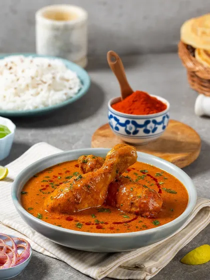 A vibrant chicken curry for Rakesh Masala. The styling includes key ingredients like red chili powder and fresh herbs to tell a story about the dish's flavor.