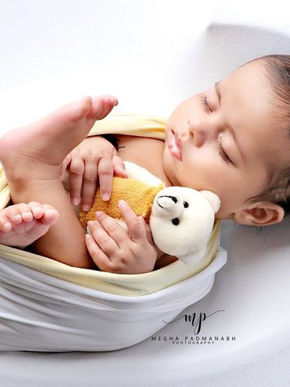 A baby boy cuddles his tiny teddy bear, swaddled in white and yellow. A simple, heartwarming portrait.