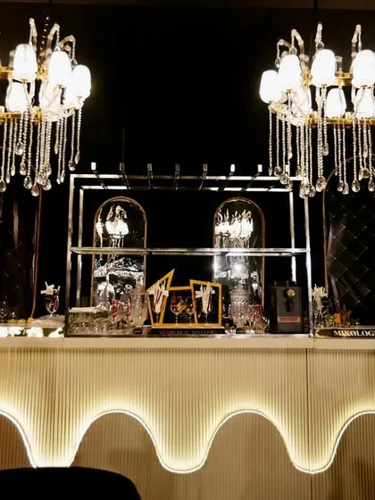 A stylish and modern bar design, featuring a scalloped, illuminated front and topped with contemporary crystal chandeliers.