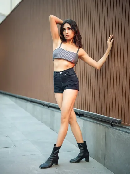 A full-body shot that showcases a modern, casual look in an urban environment. The background of clean lines and neutral tones complements the simple and stylish outfit.