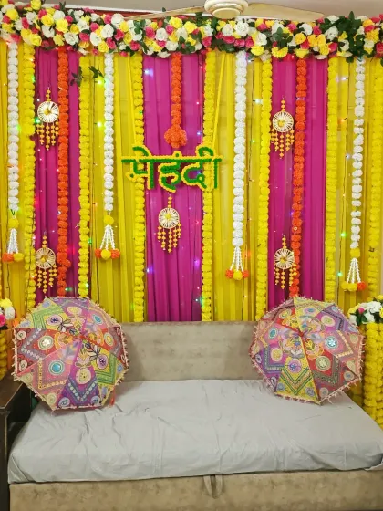 A vibrant Mehndi decor setup for a home, using yellow and pink drapes, marigold flower strings, and decorative umbrellas for a festive look.