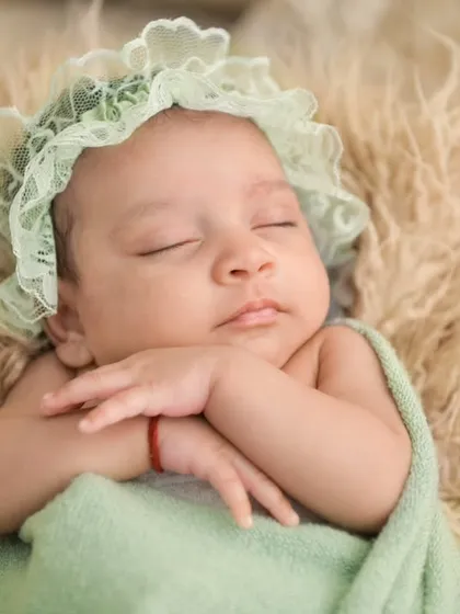 A sleeping newborn wears a delicate mint-green lace bonnet, her hands gently crossed. This image highlights our attention to detail, using soft props and accessories to add a touch of elegance to the portrait.
