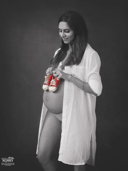 Waiting for the pitter-patter of little feet. Holding up a tiny pair of red sneakers is an adorable prop idea for a classic black and white maternity photo.