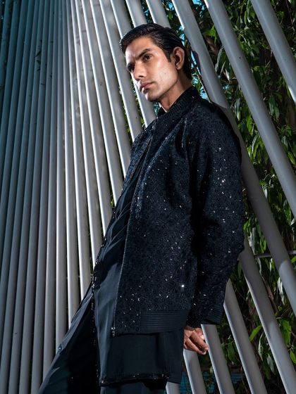 A low-angle shot emphasizing the modern silhouette of a black embellished jacket. This piece is designed for the fashion-forward man, perfect for making a statement at a New Year's Eve party or cocktail event.
