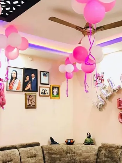A simple yet sweet "Welcome Baby Girl" decoration. The setup uses silver and pink foil balloons over a sofa, complemented by bunches of pink and white balloons.