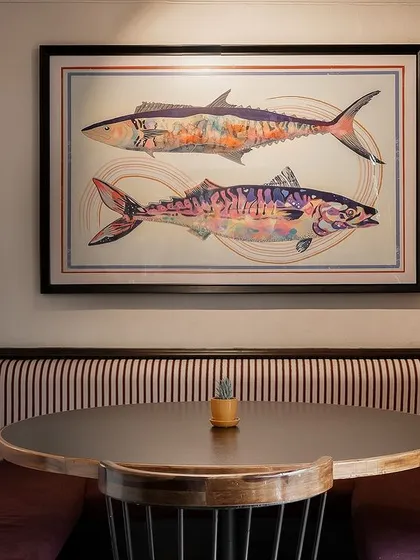 A cozy dining nook at Klaa Kitchen, featuring custom artwork of fish and striped upholstery. This intimate corner is perfect for small groups, offering a comfortable and thoughtfully designed space.