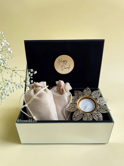 Elegance in a box. This luxe glass hamper contains fragrant potli bags and a beautiful flower-shaped brass diya, perfect as a sophisticated and minimalist Diwali gift.