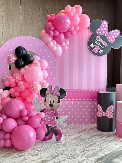A chic and modern Minnie Mouse theme for a second birthday. The setup uses bold pinks and blacks, with polka-dot and striped backdrops, a character cutout, and a stylish balloon arrangement.