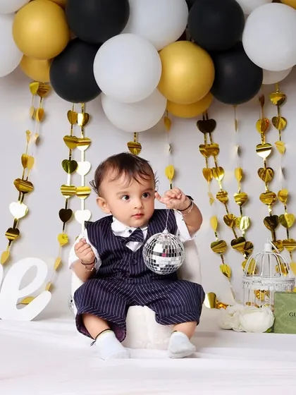 A closer look at the stylish first birthday setup, showing the little boy interacting with a disco ball prop. The gold heart streamers add a touch of glamour to the scene.