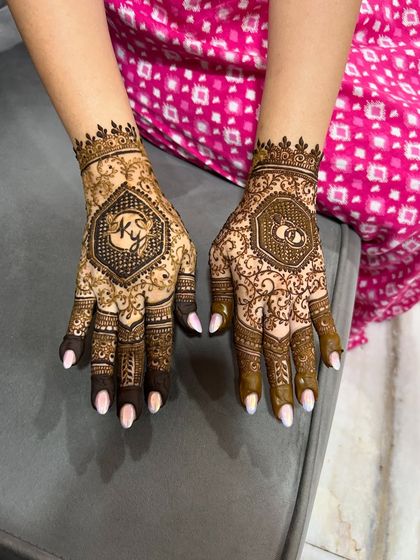 A clear view of a personalized engagement mehendi, with the couple's initials on one hand and intertwined wedding rings on the other.
