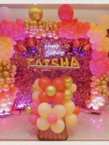 A shot of the 'Happy Birthday Taisha' party decor. The setup featured a sequin wall, a neon sign, and a beautiful balloon arch in shades of pink, yellow, and gold.