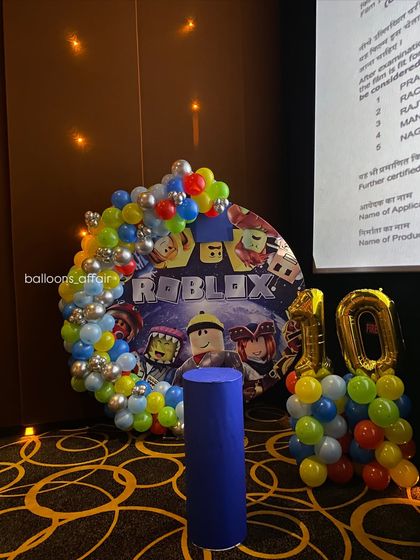 A colorful Roblox-themed birthday decoration. This setup features a custom printed backdrop with game characters, surrounded by a multi-colored balloon arch.