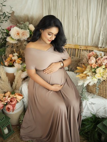 A serene portrait of a mother-to-be in a beautiful beige gown. Seated in our boho setup, she looks down at her baby bump with a gentle smile.