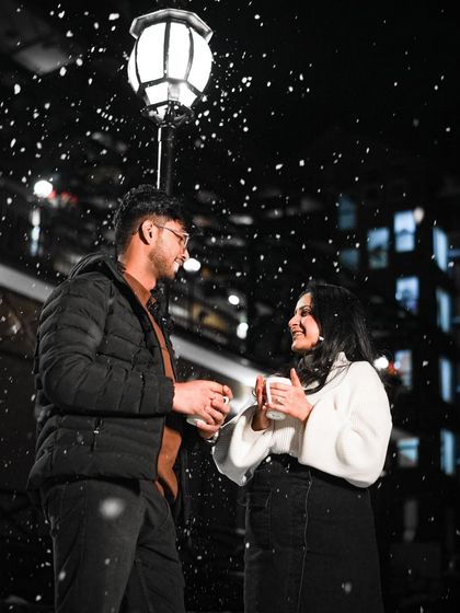 A magical night shot of a couple sharing a warm drink under falling snow in Himachal.