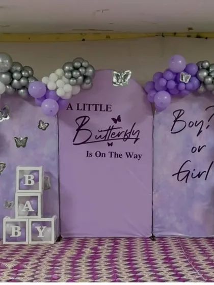 A lovely butterfly-themed baby shower or gender reveal. The backdrop asks "Boy or Girl?" and is framed by a purple, silver, and white balloon arch, creating a beautiful setting for the celebration.