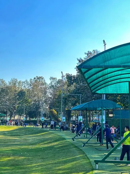 A wide shot of the driving range on a sunny day, showing the green canopies and the lush fairway.