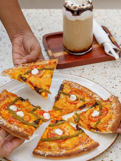 Sharing a pizza. This image captures a social, interactive moment. The focus is on the slice being taken, with its cheesy toppings and pesto drizzle. It’s a relatable and appealing shot for any pizzeria.