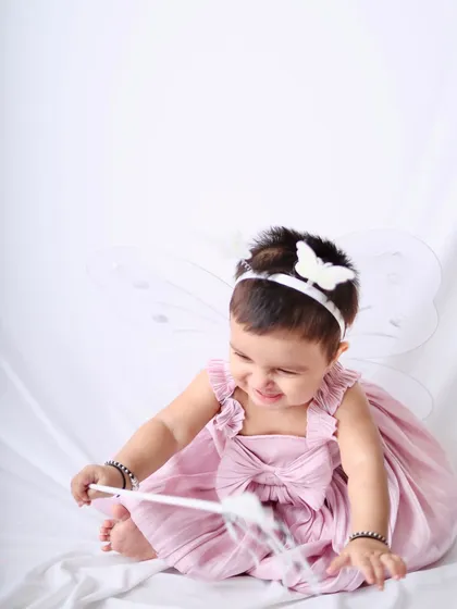A playful shot of the little fairy girl smiling as she plays with her magic wand against a simple white background.