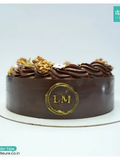 A side profile of the Chocolate Almond Nougatine cake, showcasing the clean chocolate collar and our golden 'LM' emblem.