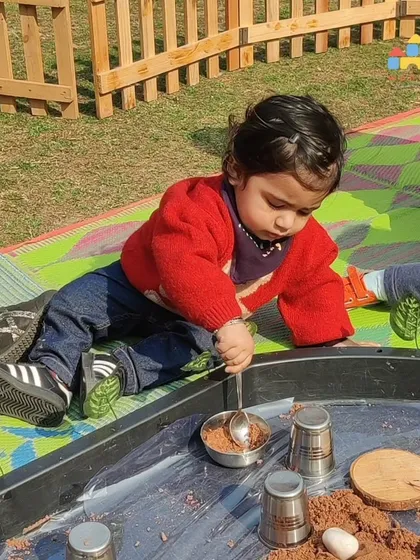 Even our youngest Cuddle Bugs get to enjoy sensory play. Here, a toddler explores the texture of a sand-like material in a safe, supervised outdoor setting, a key part of early childhood development.