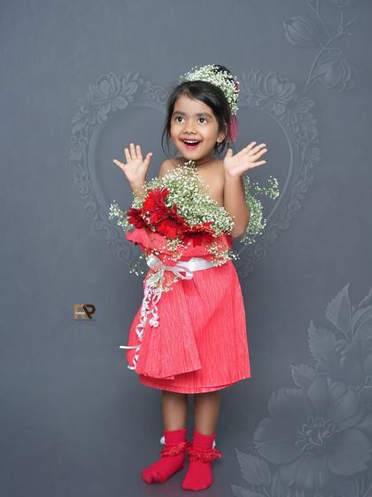 A happy girl in a flower dress, with her hands up in excitement. The simple background and beautiful outfit make for a striking and joyful portrait.