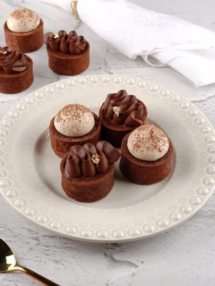 Tiny chocolate tarts with intricate piping and gold leaf details, shot to look elegant and luxurious.