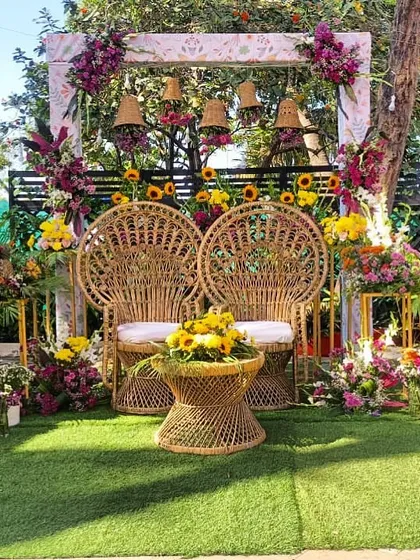 A beautiful Mehendi seating setup with bohemian-style peacock chairs. The backdrop is adorned with sunflowers and wicker bells, creating a rustic and chic vibe.