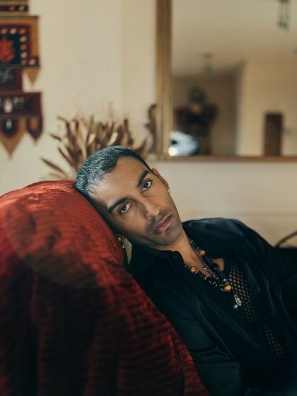 A close-up, moody portrait of artist Nilikkhimani at his home, using the rich texture of a red velvet couch to add depth.