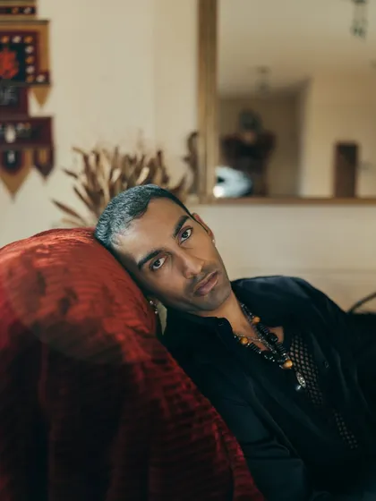 A close-up, moody portrait of artist Nilikkhimani at his home, using the rich texture of a red velvet couch to add depth.