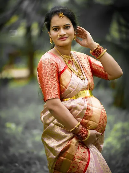 An elegant outdoor portrait of a mom-to-be in a traditional saree. The soft, out-of-focus background highlights her graceful pose and beautiful attire.
