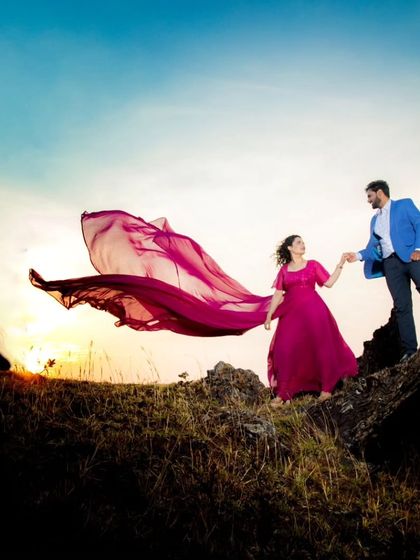 A beautiful sunset silhouette shot. The wind catches the trail of the magenta flying gown, creating a breathtakingly romantic pre-wedding photo.
