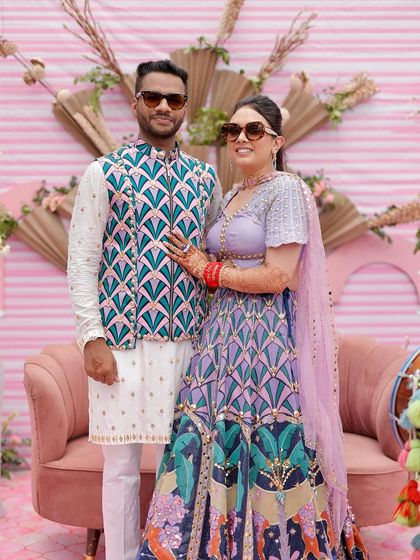 A fun and stylish couple portrait from a quirky pink Mehendi. The backdrop features dried palm fans and modern sculptural elements for a contemporary look.