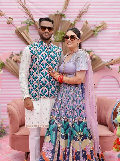 A fun and stylish couple portrait from a quirky pink Mehendi. The backdrop features dried palm fans and modern sculptural elements for a contemporary look.